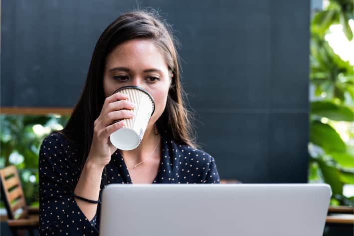 Kvinna som surfar på bärbar dator och dricker kaffe