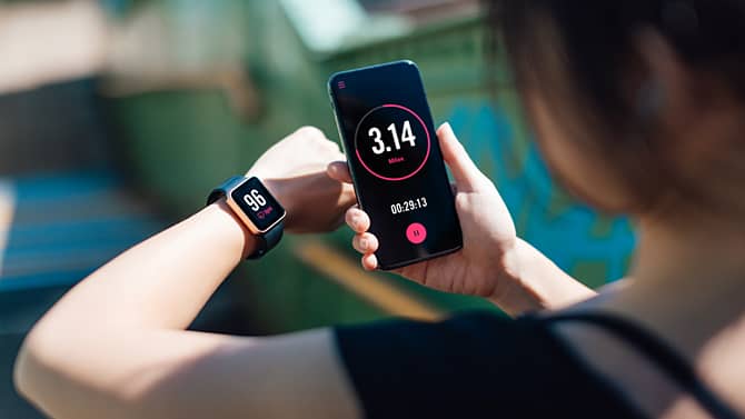En kvinna som använder en fitnessapp på sin smartphone och smartklocka. Fitnessappar är ett exempel på de positiva effekter teknik kan ha på hälsan.