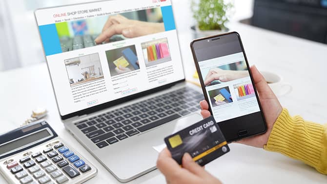 Nästan alla aktiviteter på nätet kan lämna digitala fotspår. Bilden visar en person som håller en telefon och ett kreditkort framför en datorskärm med en webbshop uppe.